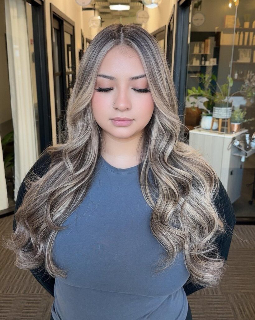 Woman showcasing long wavy ash blonde hair with delicate babylights