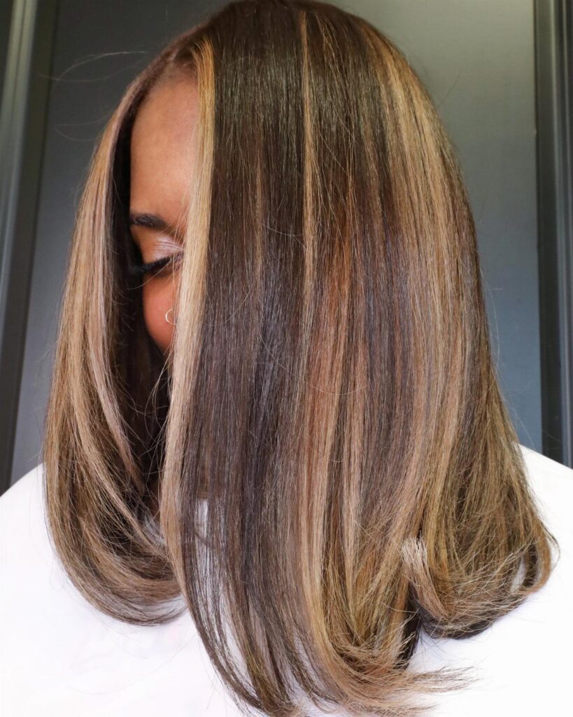 Woman showing sleek dark brown hair with caramel balayage highlights and curled ends