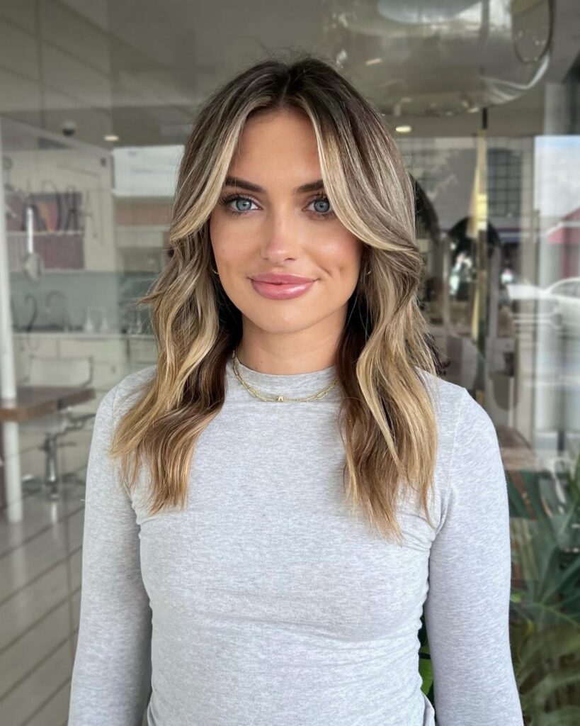 Woman with wavy dirty blonde balayage and lighter face-framing highlights