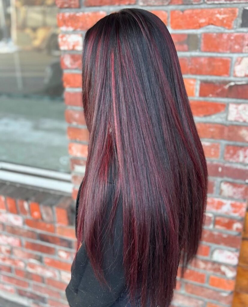 Long black hair with vivid red and burgundy highlights against a brick wall