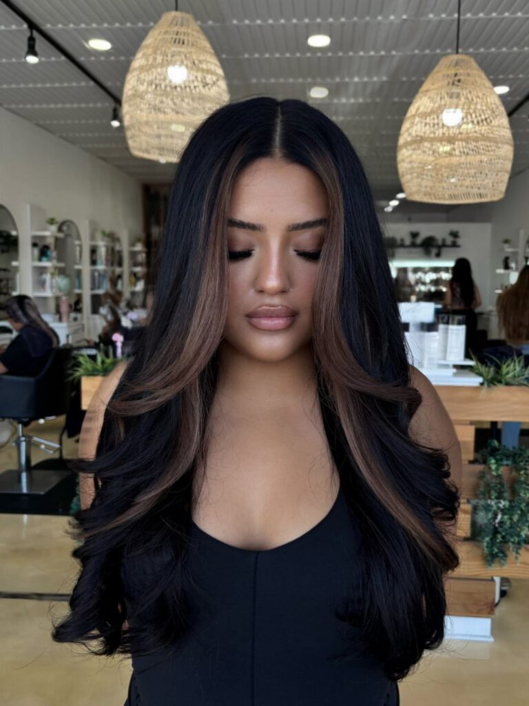 Woman with long dark waves and caramel face-framing highlights in a salon