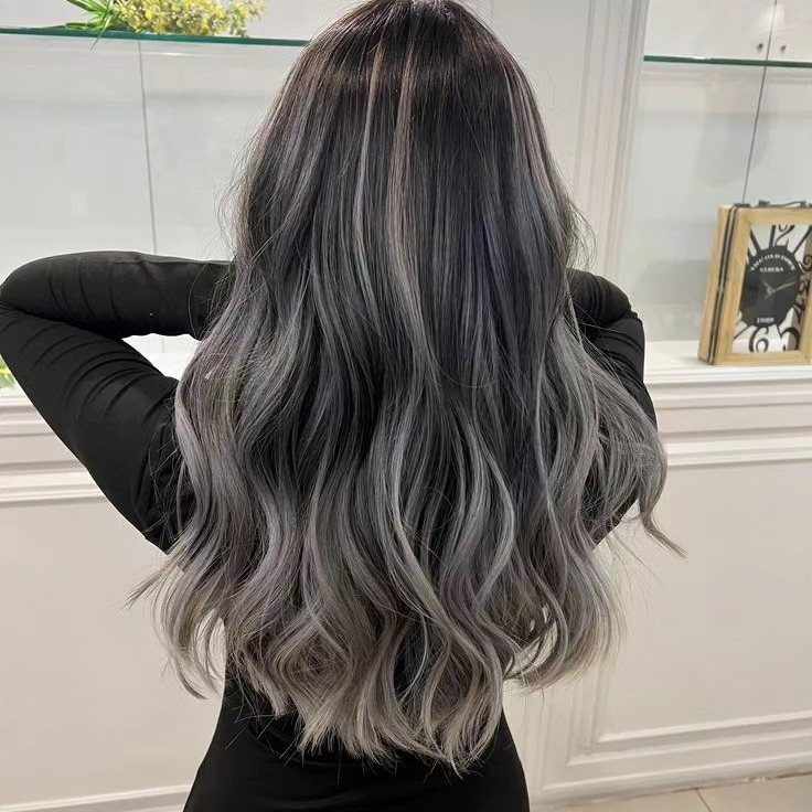 Long wavy black hair with silver-gray highlights falls down a person's back