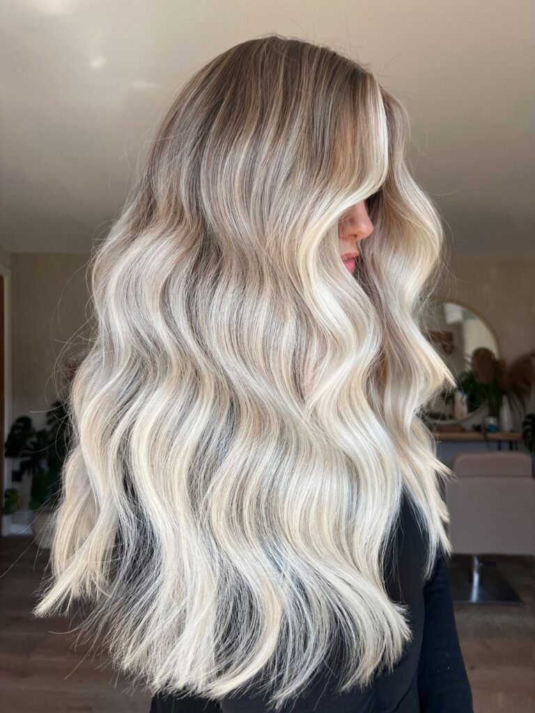 Long wavy blonde balayage hair with dark roots shown from the back