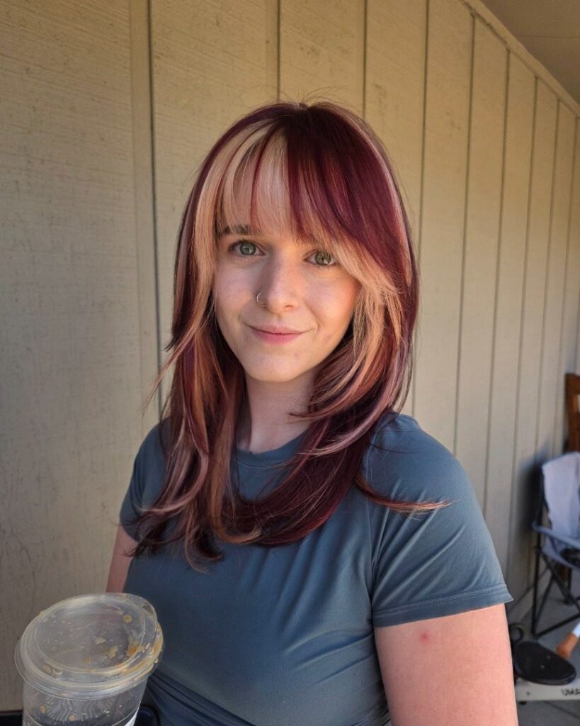 Woman with red hair and blonde highlights stands before a beige paneled wall