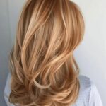 Long wavy blonde hair with warm strawberry-blonde highlights and layered curls
