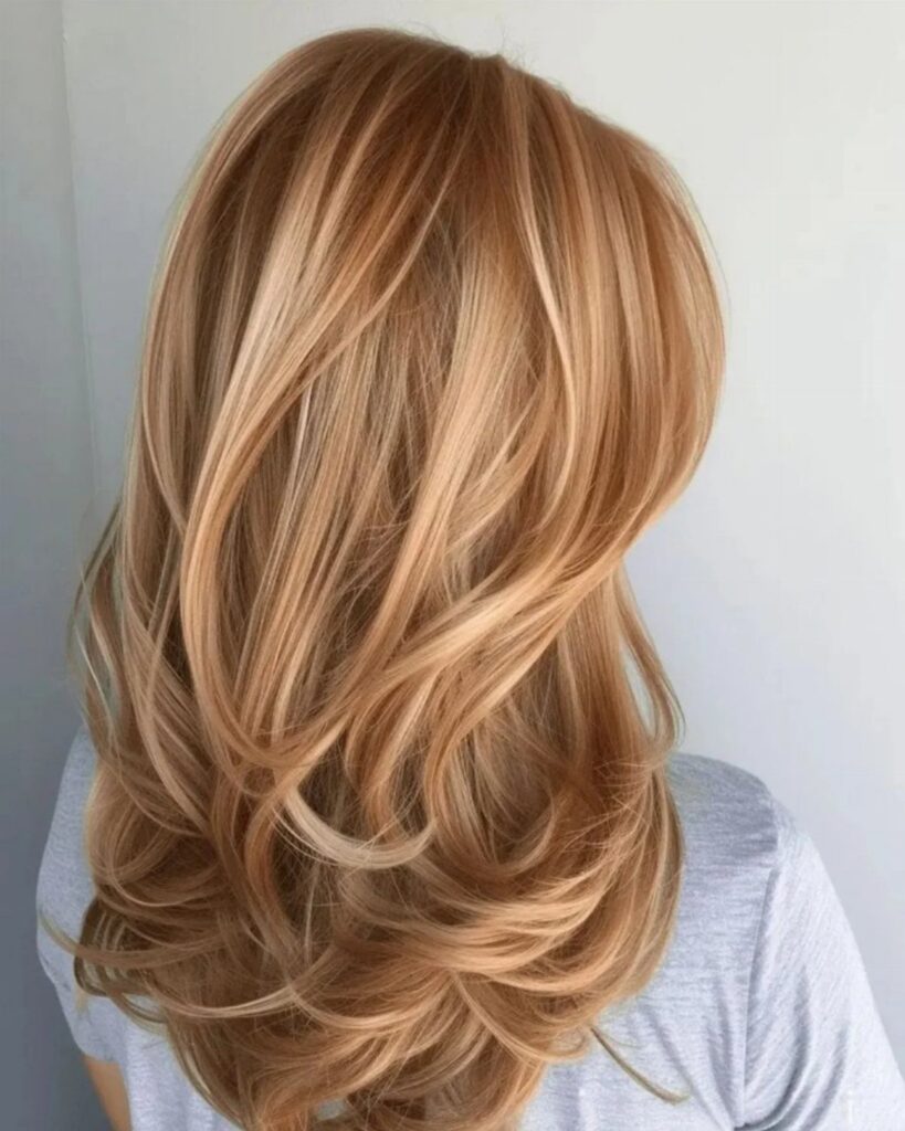 Long wavy blonde hair with warm strawberry-blonde highlights and layered curls