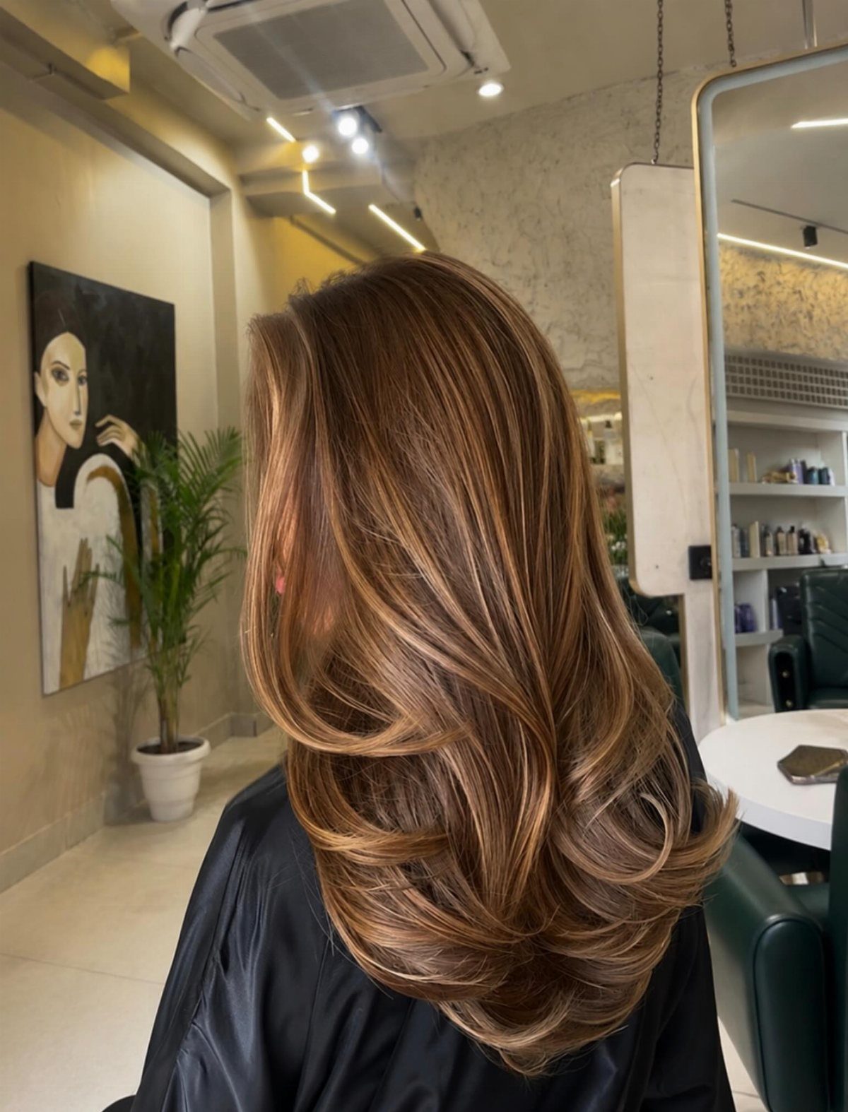 Layered brown balayage hair with caramel highlights and curled ends in a salon