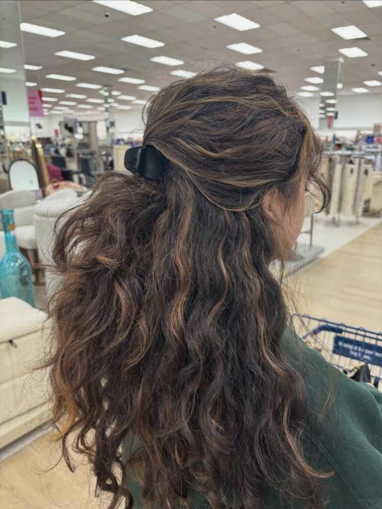 Wavy brown hair with lighter highlights partly held by a black claw clip
