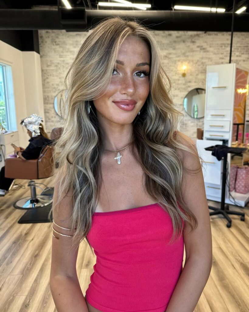 Woman showcasing wavy dirty blonde hair with lighter highlights in a salon