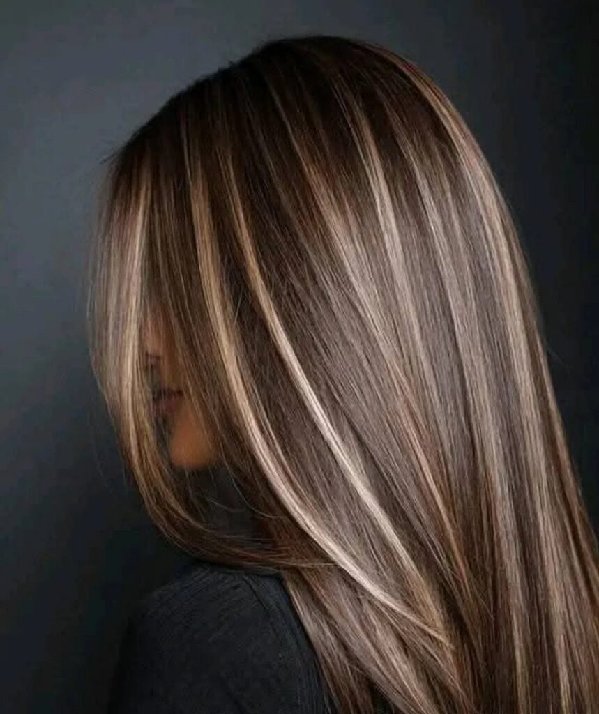 Long brown hair with bright caramel highlights against a dark background
