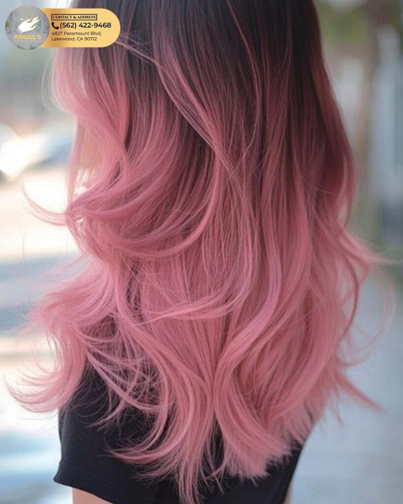 Pink ombre hair fades from dark roots into soft, curled pink ends