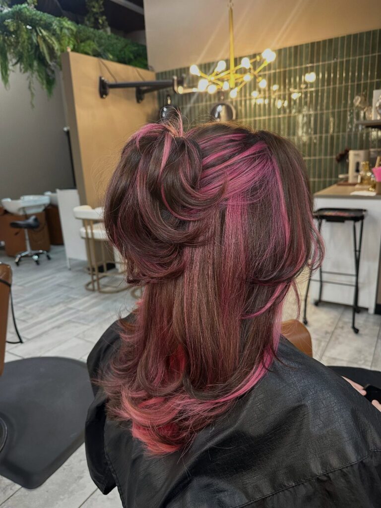 Pink-highlighted dark hair styled in loose curls at a salon