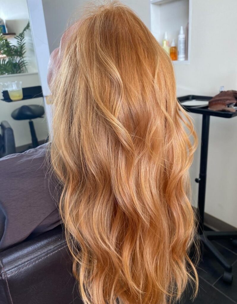 Long wavy strawberry blonde hair with lighter highlights in a salon